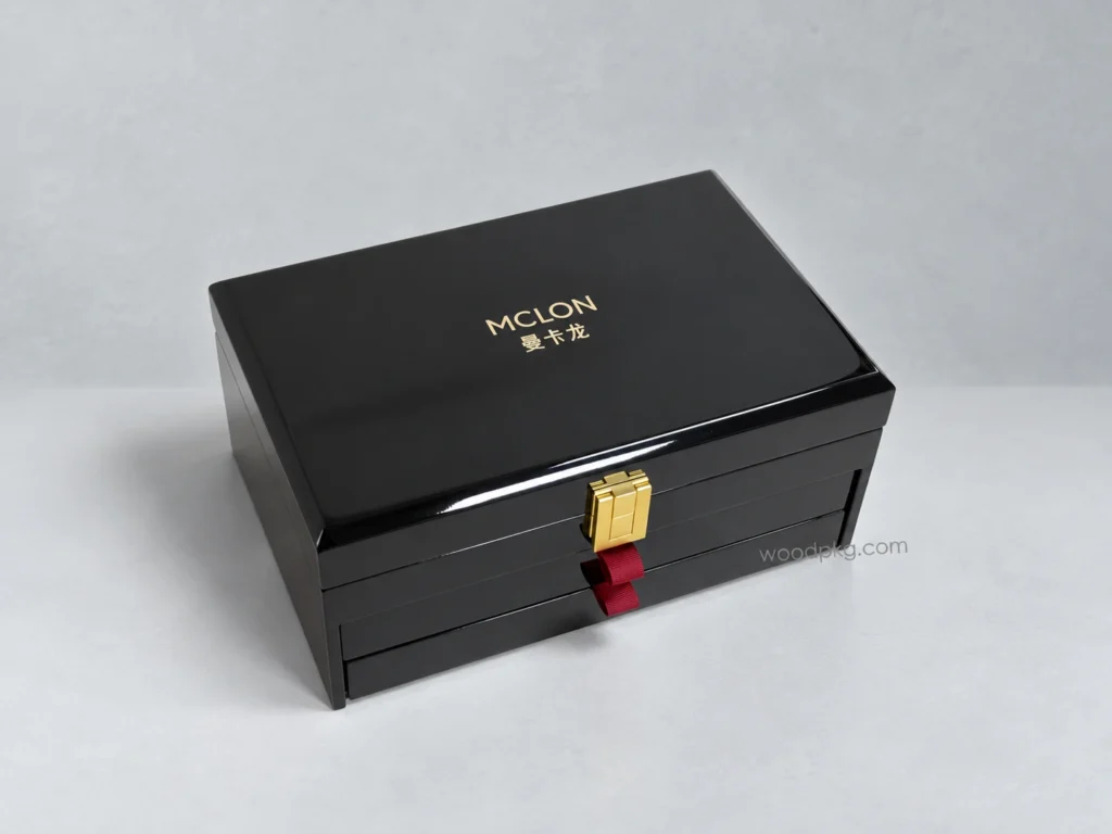 Custom black high-gloss wooden jewelry box with multiple storage layers, a gold-tone clasp, and red ribbon drawer pulls.